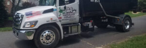 A white dump truck parked on a residential street with contact information and American flag decals on the side.