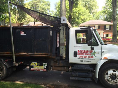 A white truck with "A1 Clean-Up" on the side is parked on a residential street, carrying a large black dumpster.